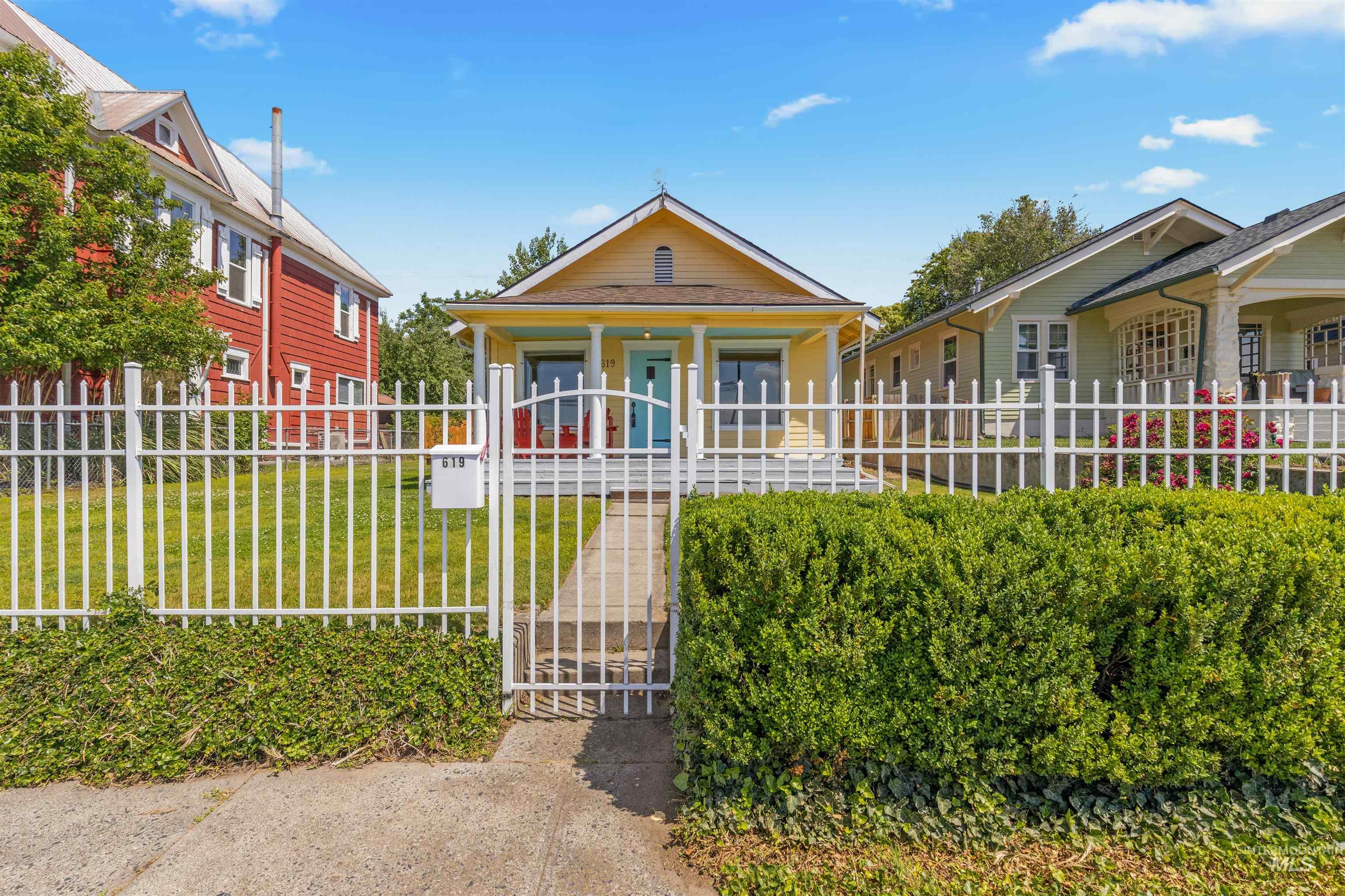 619 Prospect Avenue Lewiston, ID 83501 - Photo 5 of 37 Charming bungalow featuring a bright yellow exterior, white picket fence, mature front hedge, and a vibrant turquoise front door