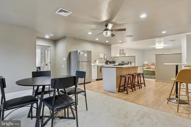 a kitchen with stainless steel appliances kitchen island granite countertop a dining table chairs and a refrigerator