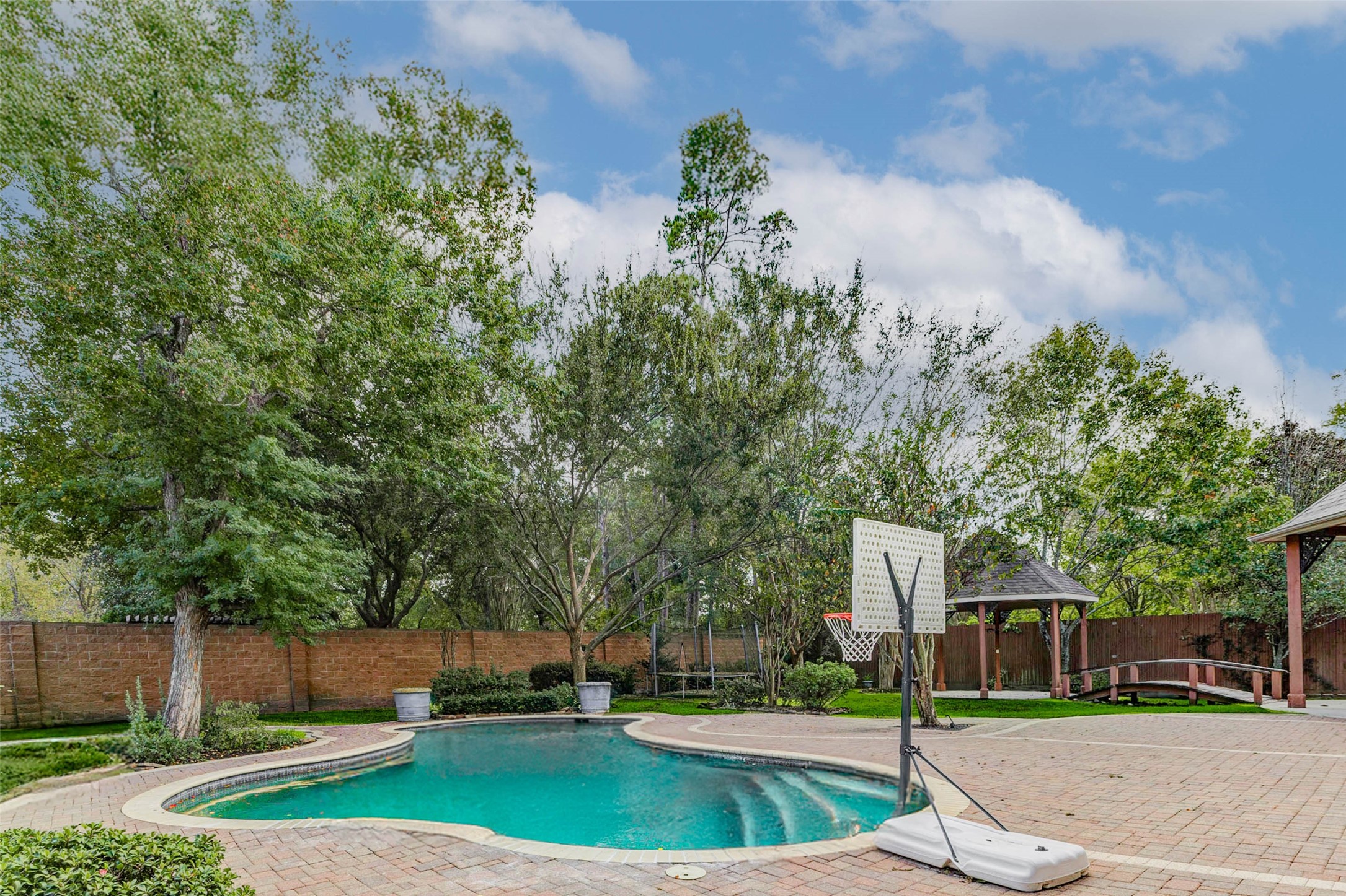 3509 Mirror Court Spring, TX 77388 - Photo 35 of 45 The sparkling pool is surrounded by mature trees and beautifully maintained landscaping, creating a peaceful and private setting. There’s plenty of deck space for lounging, plus room for outdoor activities like basketball or relaxing under the nearby gazebo.