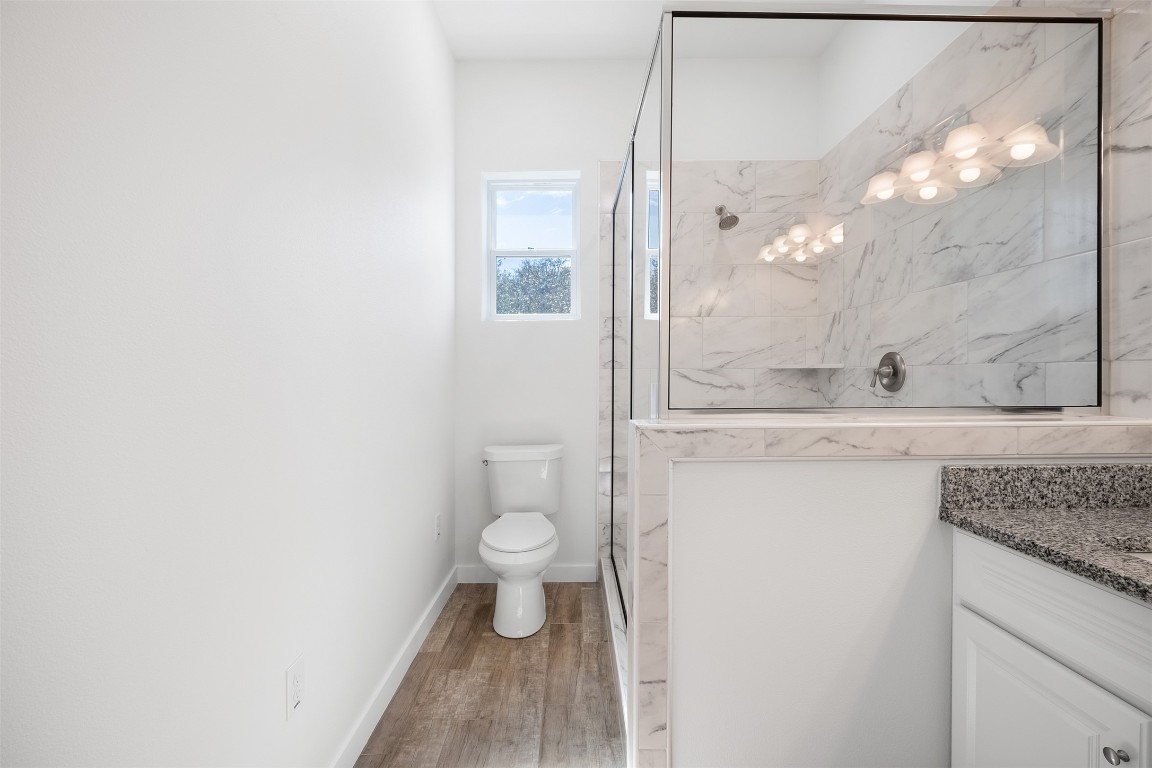 255 Lourdes Court, Unit A Dripping Springs, TX 78620 - Photo 16 of 27 a bathroom with a granite countertop sink a toilet and a mirror