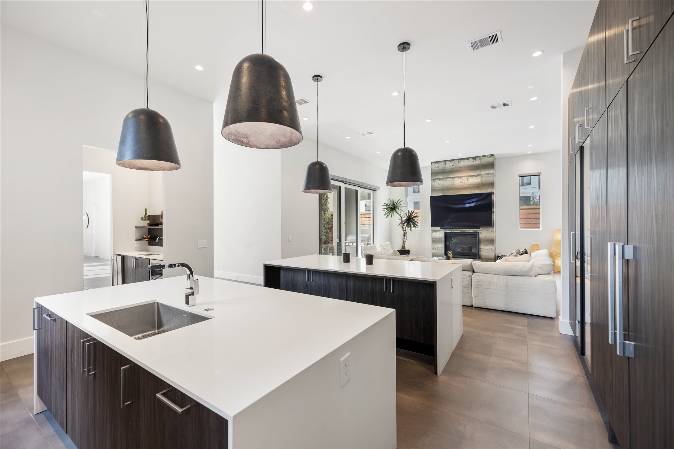 103 Roy Street Houston, TX 77007 - Photo 12 of 37 Dual waterfall-edge islands anchor the chef’s kitchen while maintaining open sightlines to the main living area and private pool courtyard. Statement pendant lighting and streamlined cabinetry reinforce the home’s cohesive contemporary design.