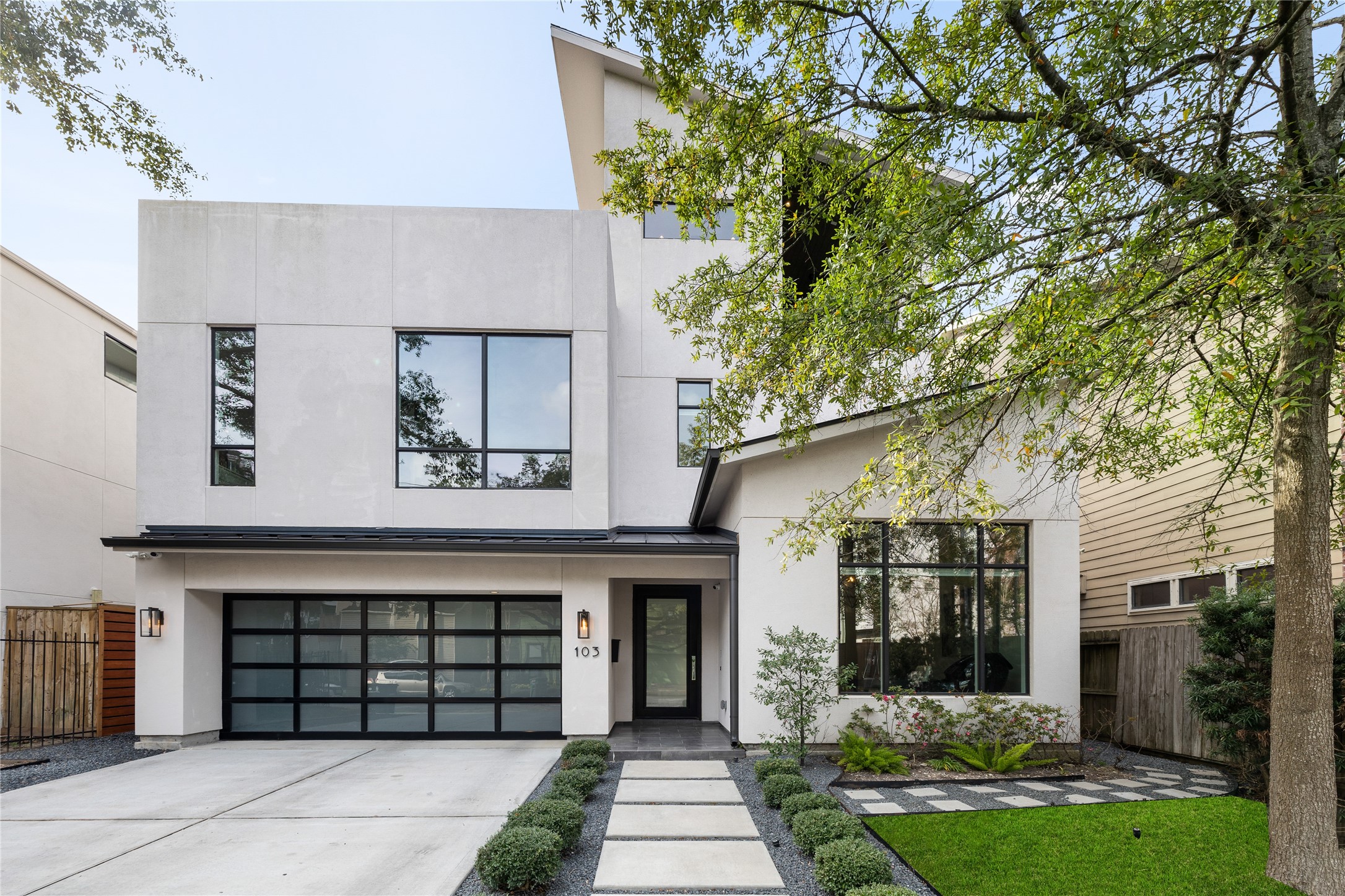 103 Roy Street Houston, TX 77007 - Photo 2 of 37 Balanced contemporary composition showcasing clean lines, expansive window placements, and a refined neutral palette. Modern glass-panel garage door, structured walkway approach, and understated landscaping complement the home’s architectural simplicity while enhancing curb presence.