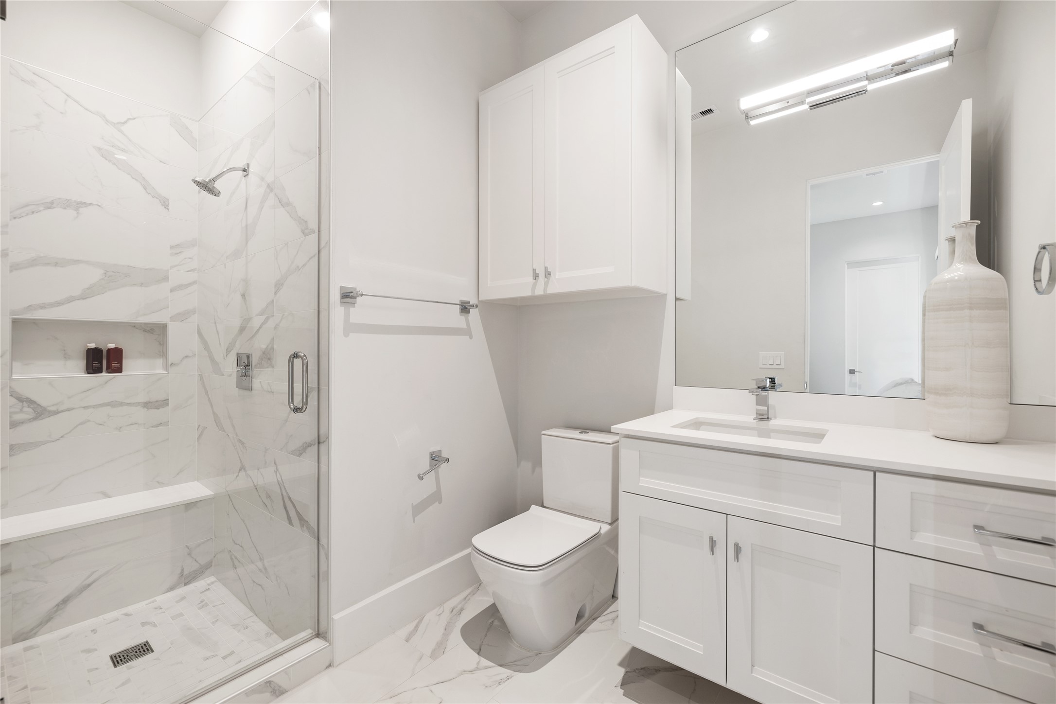 103 Roy Street Houston, TX 77007 - Photo 29 of 37 Beautifully appointed full bath showcasing marble tile, frameless glass walk-in shower, and clean-lined vanity with contemporary fixtures — offering a bright, polished, and timeless aesthetic.