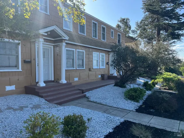 a view of a brick house with many windows plants and large trees