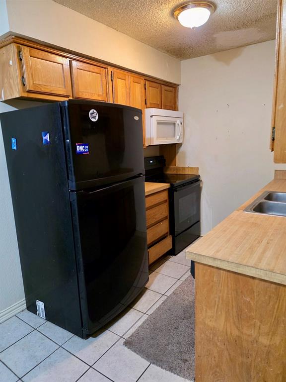 922 Fannin Street, Unit 102 Denton, TX 76201 - Photo 3 of 9 Kitchen featuring light tile patterned floors, brown cabinetry, light countertops, a textured ceiling, and black appliances