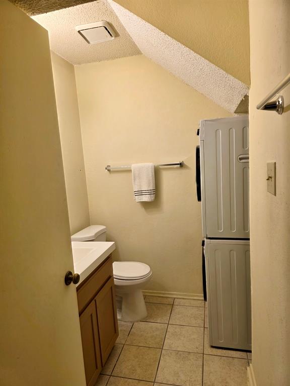922 Fannin Street, Unit 102 Denton, TX 76201 - Photo 5 of 9 Bathroom featuring stacked washer and dryer, visible vents, toilet, vanity, and tile patterned floors