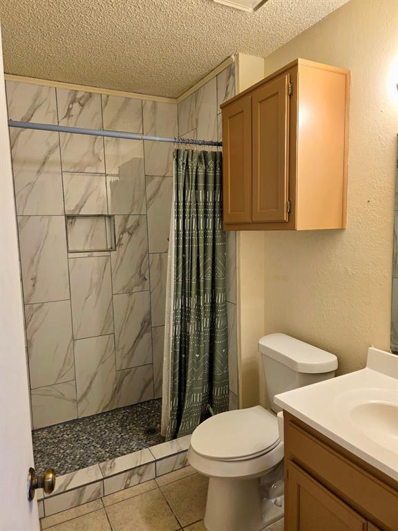 922 Fannin Street, Unit 102 Denton, TX 76201 - Photo 7 of 9 Bathroom featuring a textured wall, toilet, a stall shower, a textured ceiling, and vanity