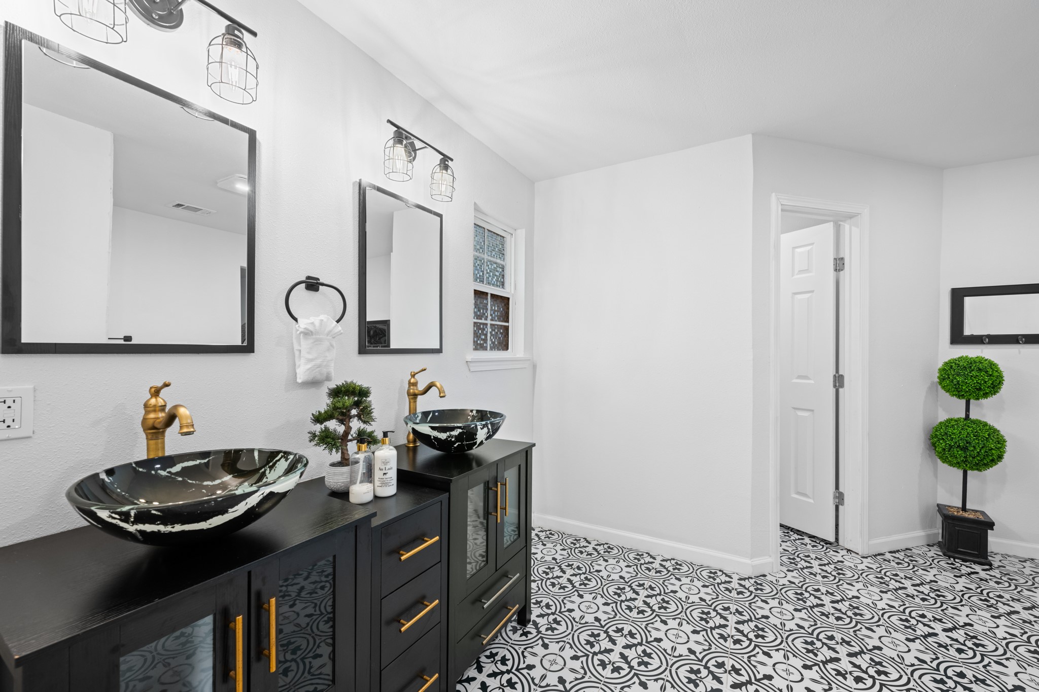 729 Kyle Angleton, TX 77515 - Photo 24 of 36 This modern bathroom features a stylish double vanity with vessel sinks, brass fixtures, and elegant black cabinetry. The floor showcases intricate black-and-white patterned tiles, and the room is well-lit with contemporary lighting.
