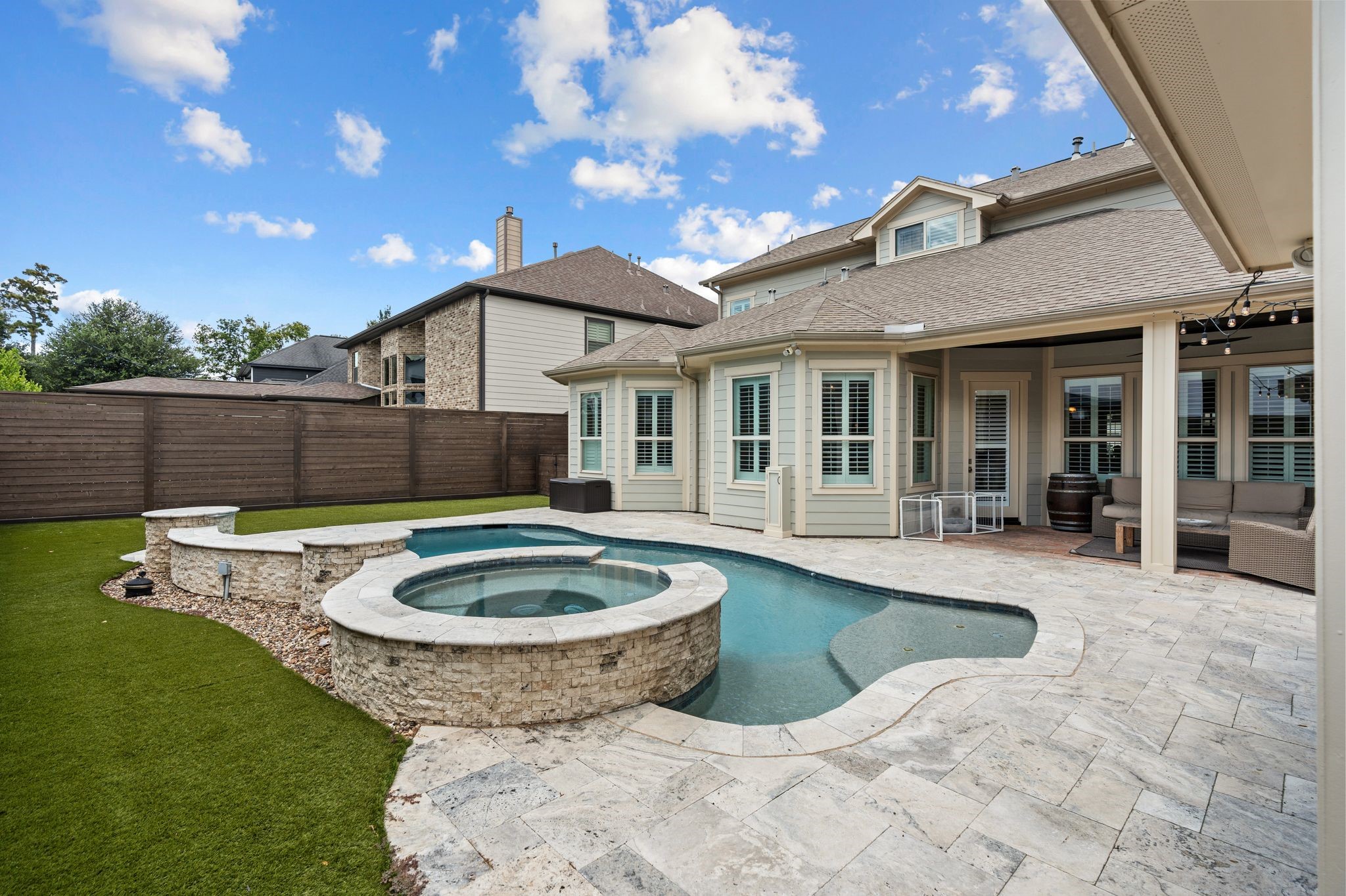 1217 Chippendale Road Houston, TX 77018 - Photo 39 of 42 Expansive travertine decking surrounds the pool & spa, providing abundant room for lounge seating & effortless entertaining. Low-maintenance turf, string lighting, outdoor speakers, & a newer backyard fence ('25) enhance this private outdoor retreat.