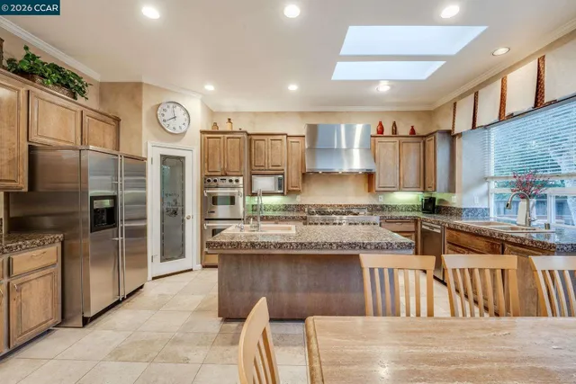 a kitchen with stainless steel appliances granite countertop a stove top oven a sink dishwasher a dining table and chairs with wooden floor