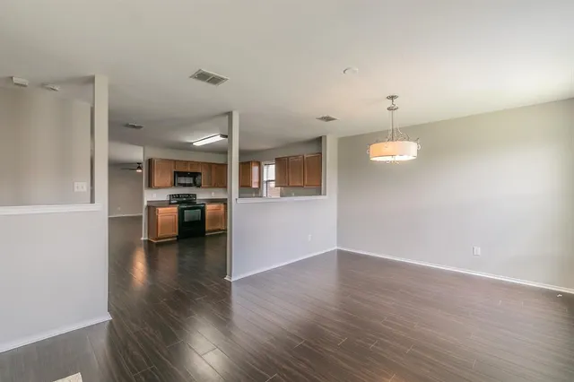 an empty room with wooden floor and kitchen view