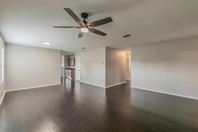 a view of an empty room with wooden floor and a ceiling fan