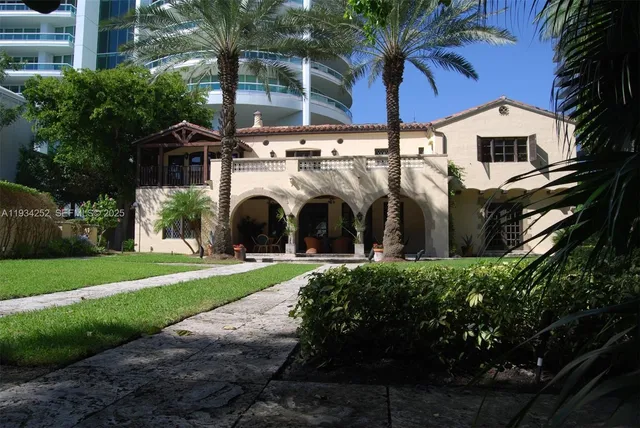 a view of a white house with a large tree and a yard in front of it