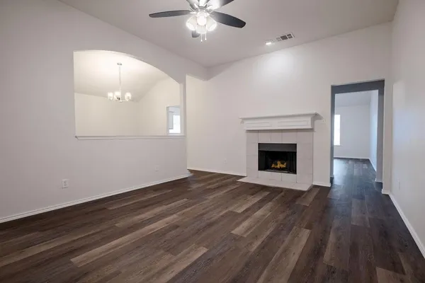 an empty room with wooden floor a ceiling fan a fireplace and windows