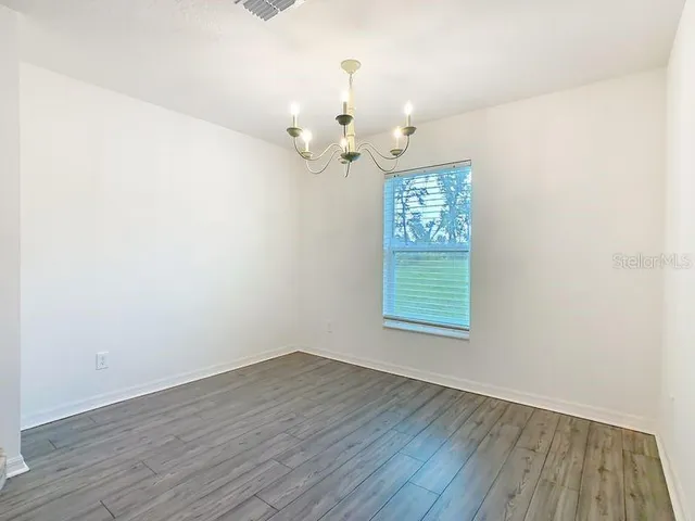 an empty room with wooden floor chandelier fan and windows