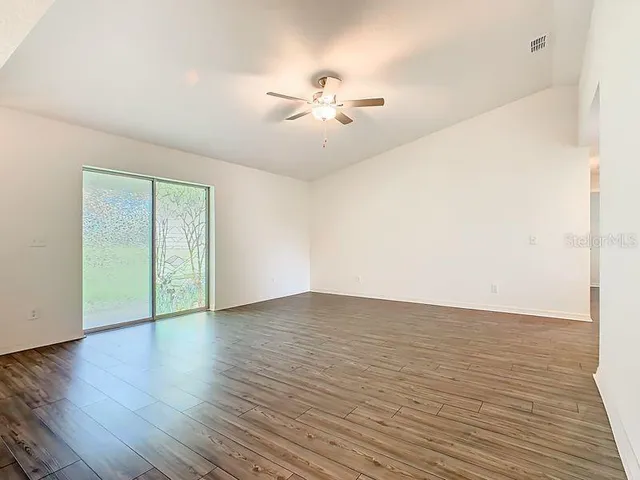 a view of an empty room with wooden floor and a ceiling fan