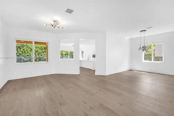 an empty room with wooden floor chandelier and windows