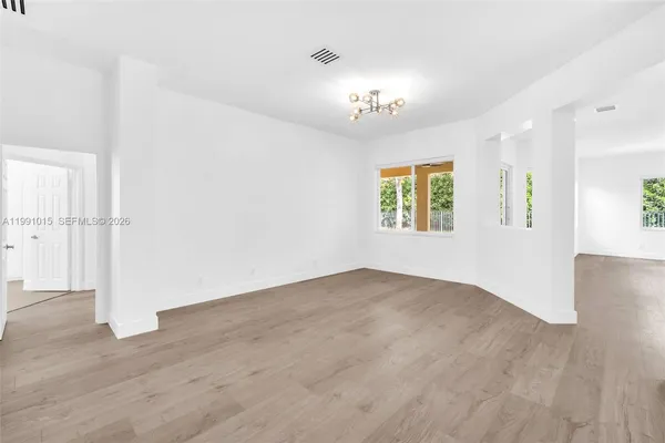 an empty room with wooden floor chandelier and windows
