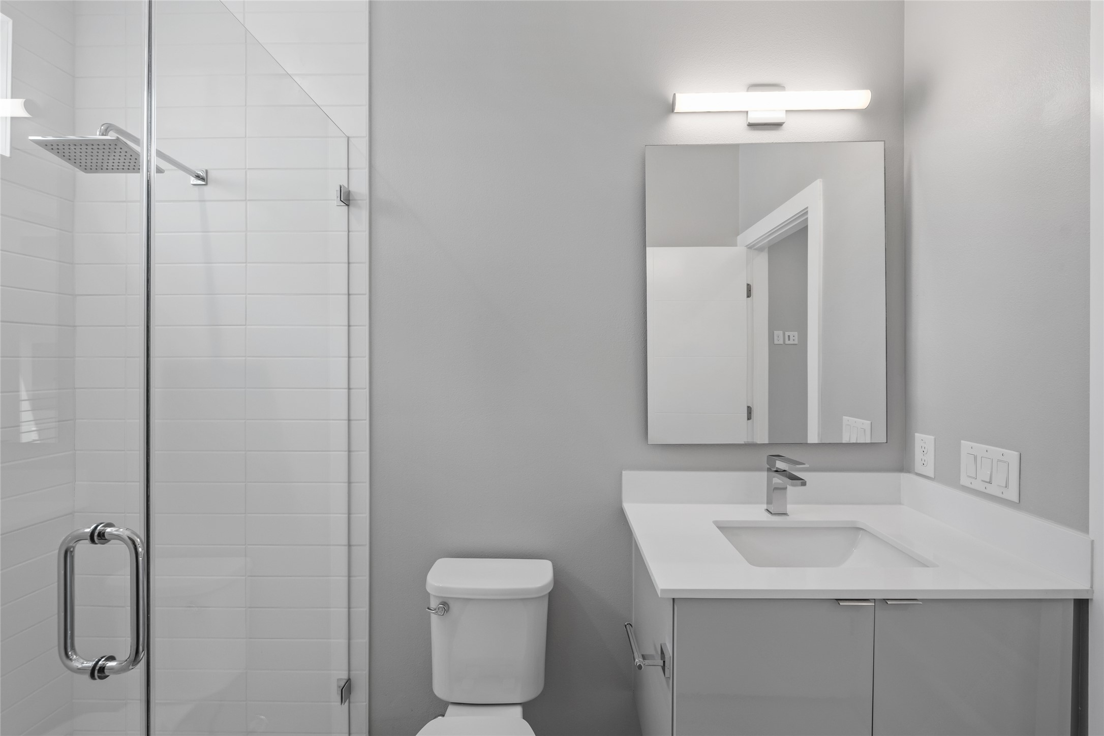 2108 Tillery Street, Unit 16 Austin, TX 78723 - Photo 13 of 15 Contemporary bathroom featuring a frameless glass shower enclosure, a square rain showerhead, a toilet, a vanity with a white countertop and integrated sink, and a rectangular mirror with an overhead light fixture