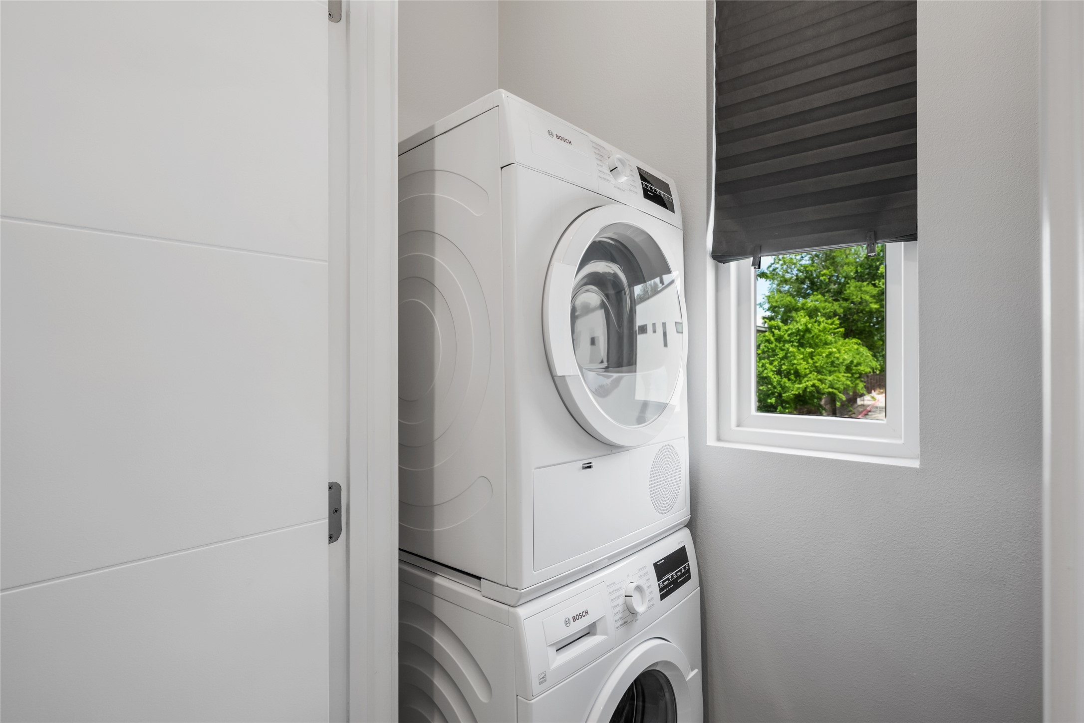 2108 Tillery Street, Unit 16 Austin, TX 78723 - Photo 15 of 15 Dedicated laundry area featuring a stacked washer and dryer unit, a white-framed window with a grey pleated blind, and a modern white panel door