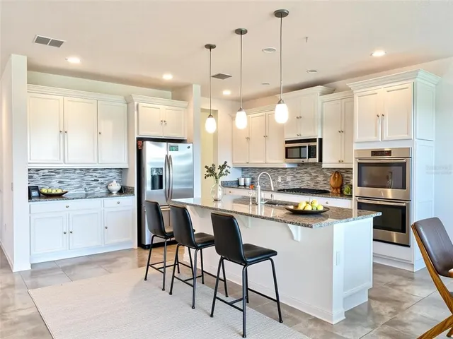 a kitchen with stainless steel appliances a stove a sink a refrigerator white cabinets and chairs