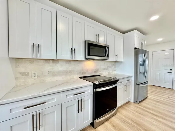 a kitchen with stainless steel appliances granite countertop white cabinets a sink a stove a refrigerator and microwave with wooden floor