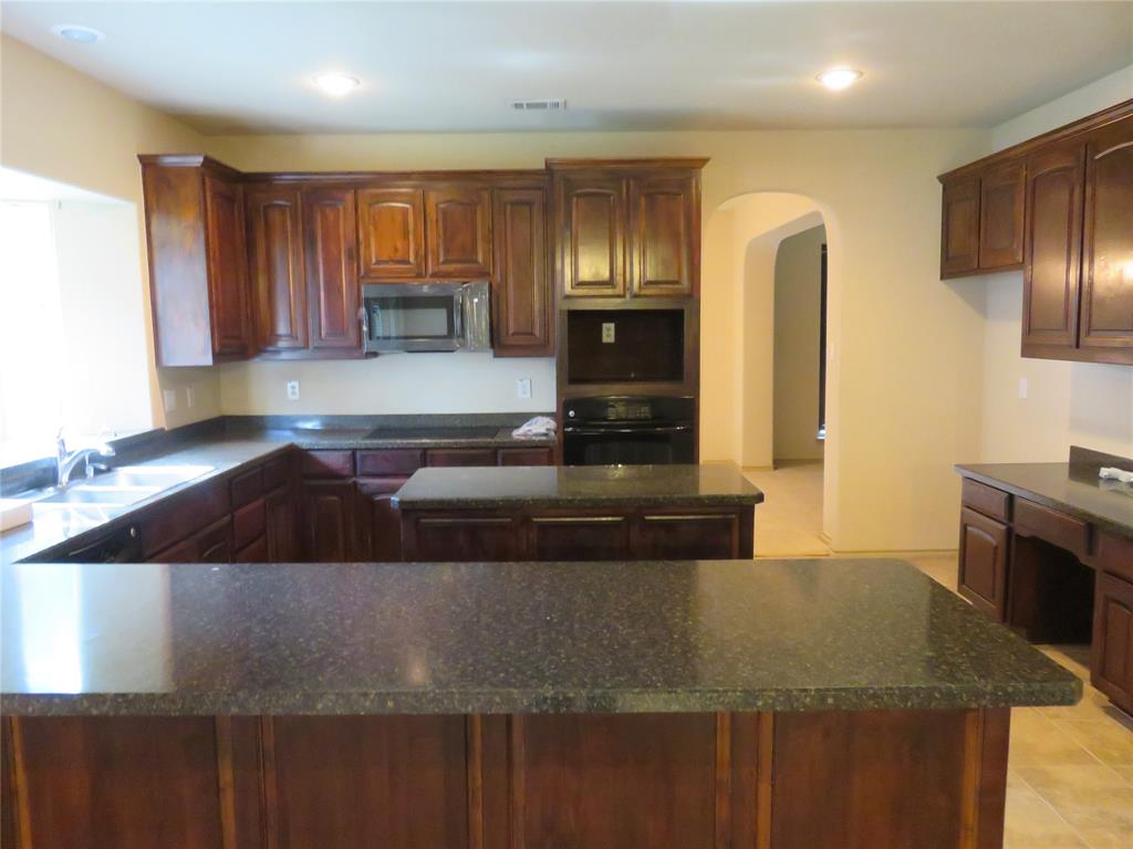 1122 Walter Stephenson Road Midlothian, TX 76065 - Photo 8 of 26 Kitchen featuring dark wood cabinetry, speckled countertops, a double basin sink, built-in microwave, and arched doorway