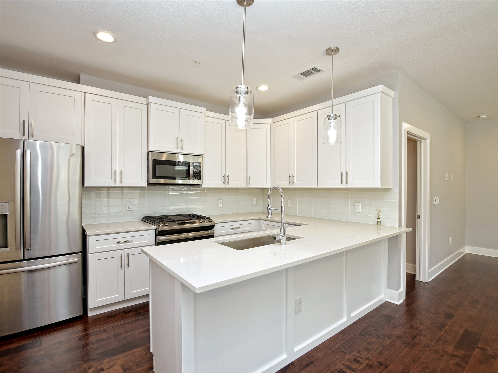 1130 Lott Avenue, Unit B Austin, TX 78721 - Photo 10 of 29 Kitchen with stainless steel appliances, white cabinetry, hanging light fixtures, and dark wood-style flooring