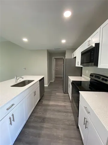 a large white kitchen with a sink and dishwasher a stove top oven with wooden floor