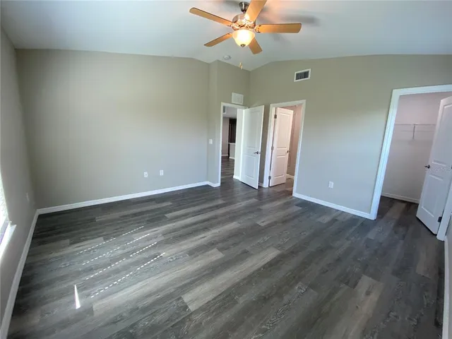 an empty room with wooden floor fan and windows