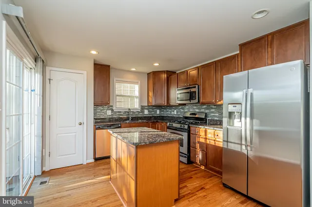 a kitchen with stainless steel appliances granite countertop a refrigerator a stove and a sink with wooden floor