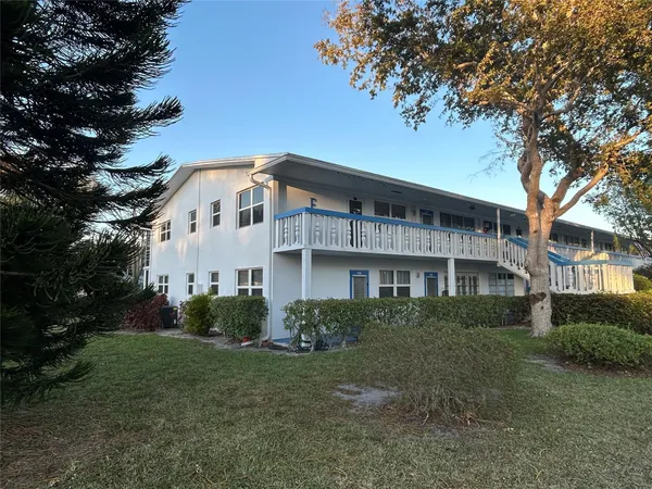 a view of a white house next to a yard with plants and trees