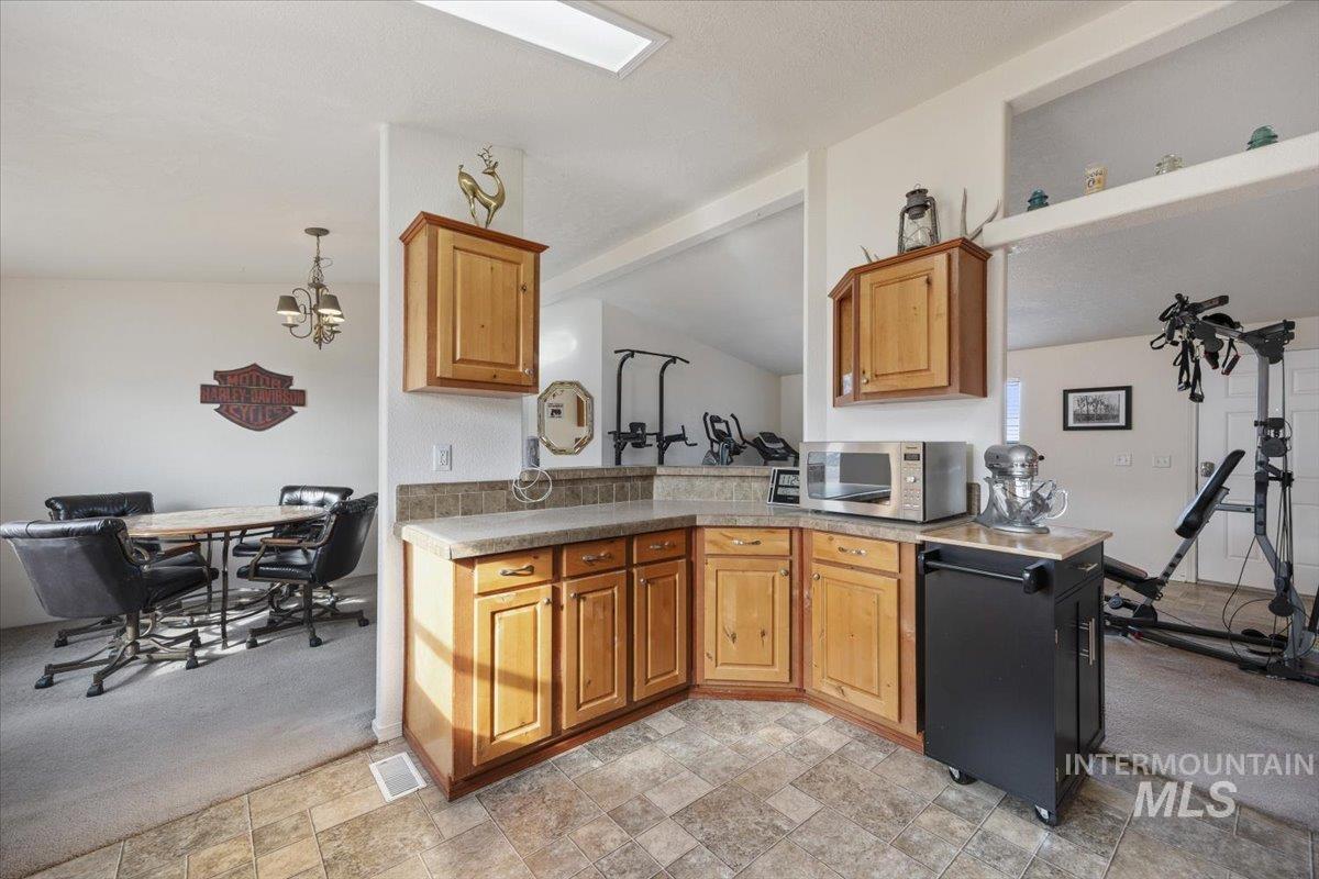 1014 S Highway Albion, ID 83311 - Photo 10 of 34 Kitchen featuring light colored carpet, stone finish floors, stainless steel microwave, lofted ceiling, and wood finish cabinetry