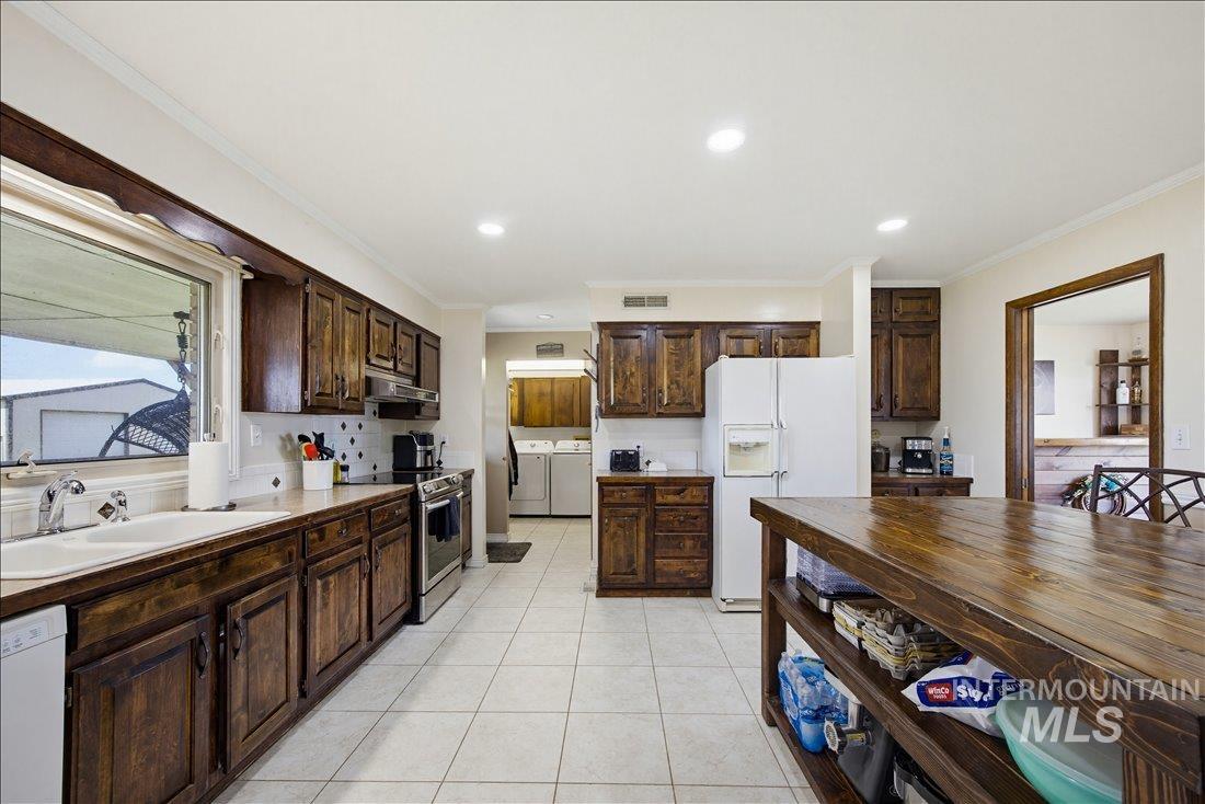 1901 South Ten Mile Road Meridian, ID 83642 - Photo 10 of 32 Spacious kitchen featuring extensive dark wood cabinetry, white tile flooring, a large window over the sink, recessed lighting, and stainless steel appliances
