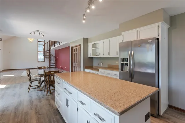 a large kitchen with stainless steel appliances a large counter top a stove a refrigerator white cabinets and wooden floor