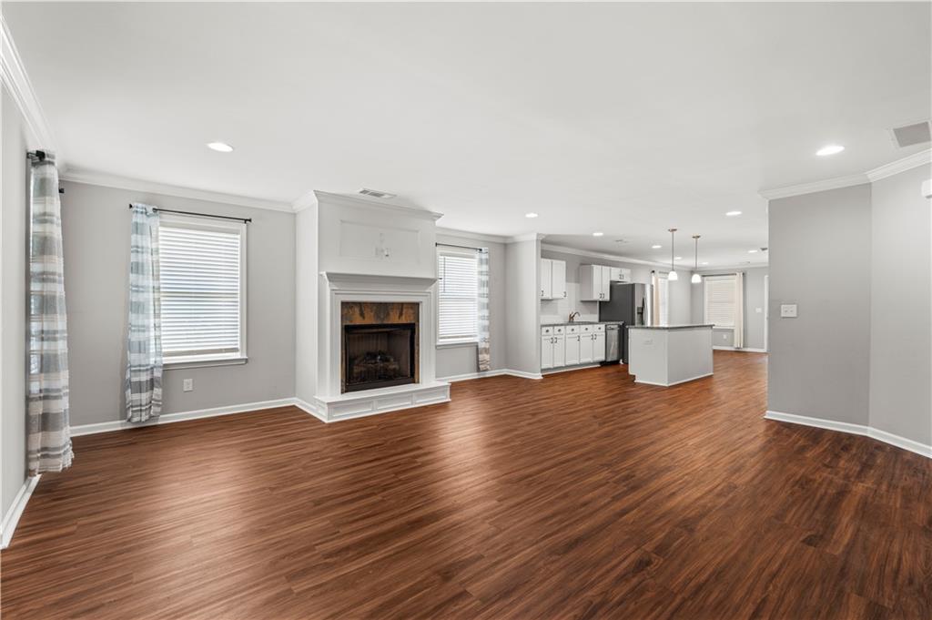 Open-concept living space featuring wood-finish flooring, a white mantel fireplace, and recessed lighting