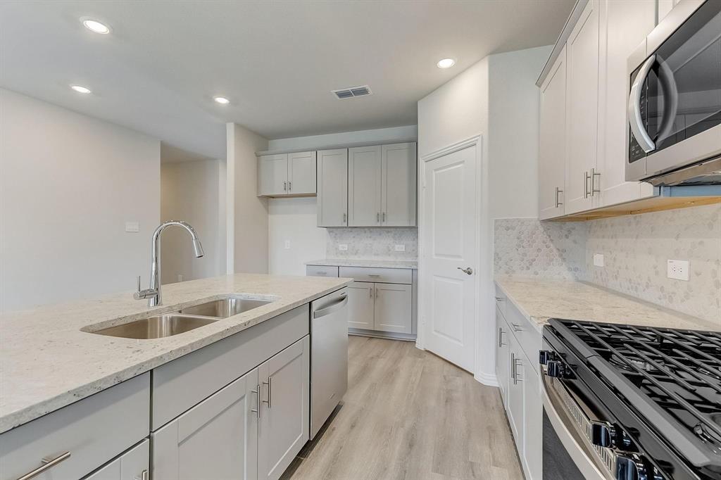 1405 Winters Way McKinney, TX 75071 - Photo 6 of 32 Kitchen featuring appliances with stainless steel finishes, sink, decorative backsplash, light hardwood / wood-style floors, and light stone countertops