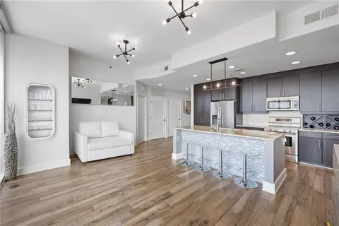 a large white kitchen with kitchen island a chandelier stainless steel appliances cabinets and wooden floor