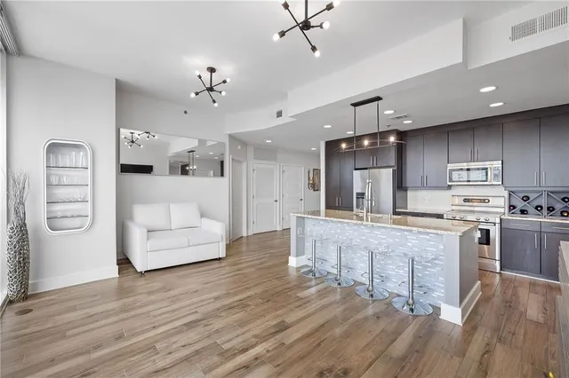 a large white kitchen with kitchen island a chandelier stainless steel appliances cabinets and wooden floor