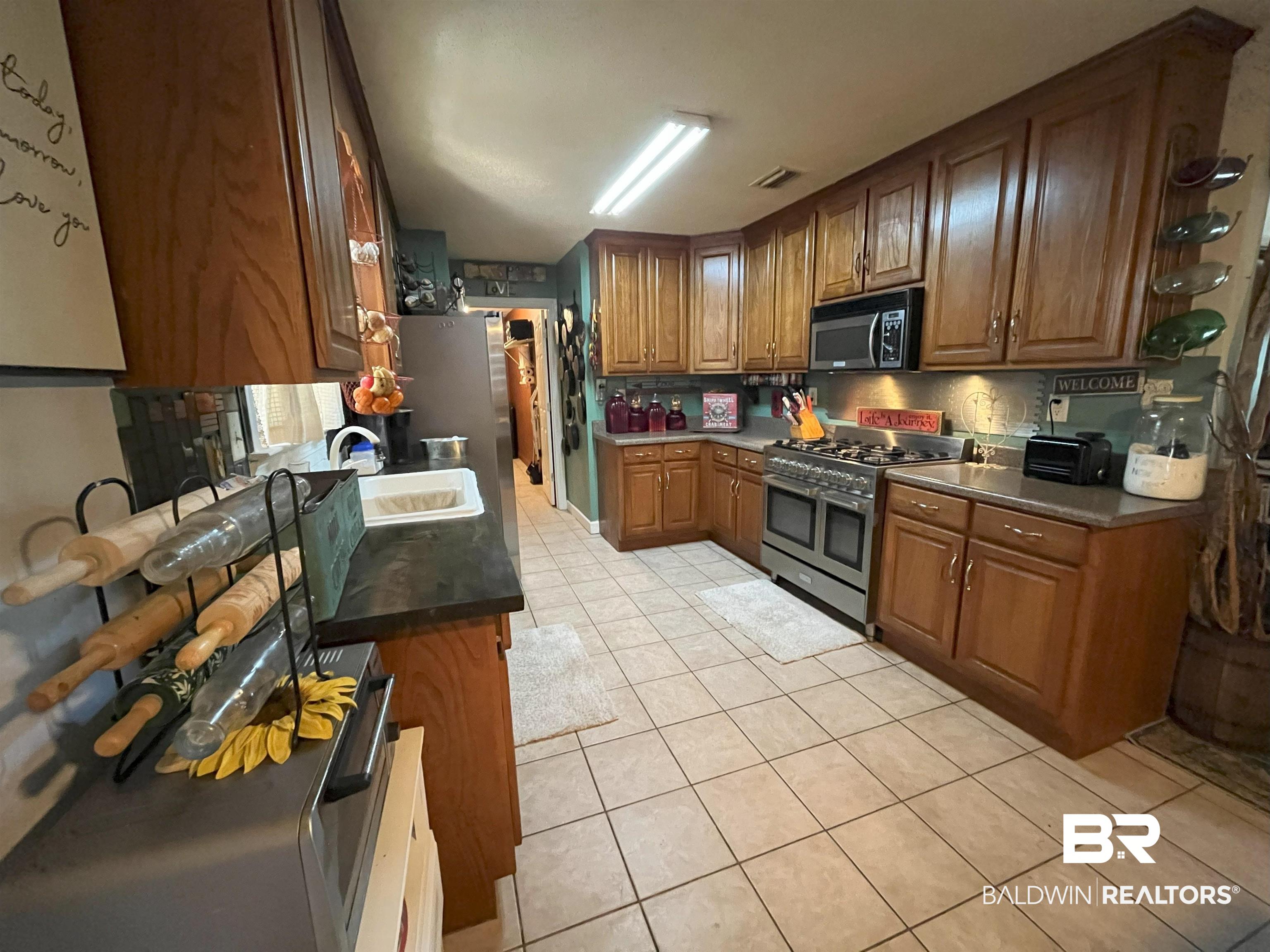 7851 Highway 98 Fairhope, AL 36532 - Photo 17 of 40 Kitchen featuring dark countertops, appliances with stainless steel finishes, light tile patterned floors, and brown cabinetry