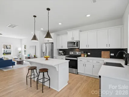 a kitchen with a stove a sink a kitchen island with chairs and white cabinets