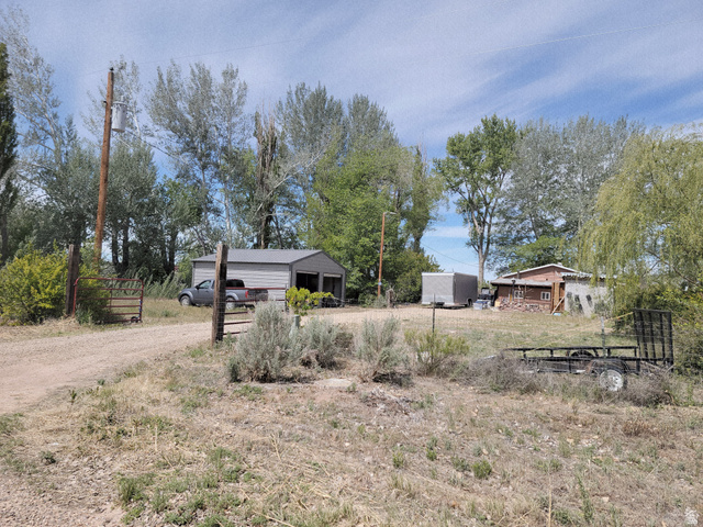 10429 4th Street East Randlett, UT 84063 - Photo 1 of 19 Gated property entrance with a gravel driveway, featuring a two-bay detached garage with a metal roof, and an additional storage structures