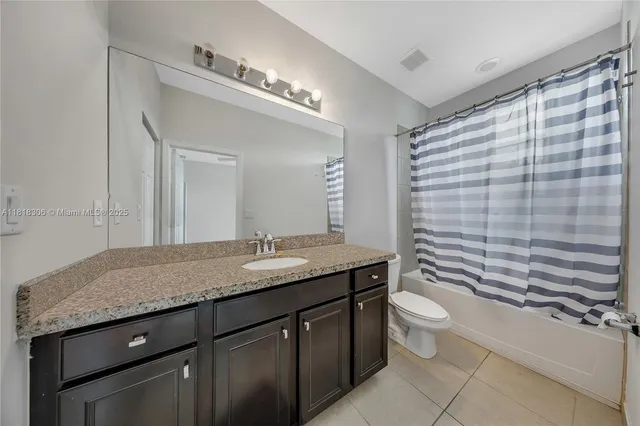 a bathroom with a granite countertop sink a toilet a mirror and shower curtain