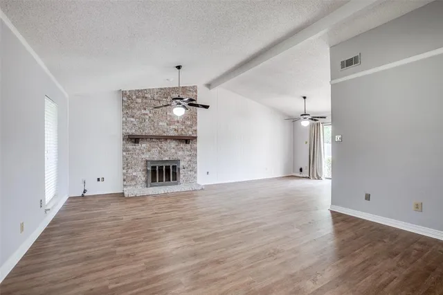 an empty room with wooden floor fireplace and chandelier