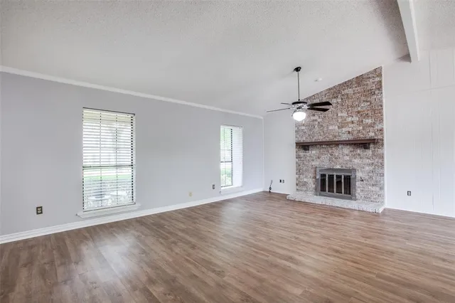 an empty room with wooden floor fireplace and windows