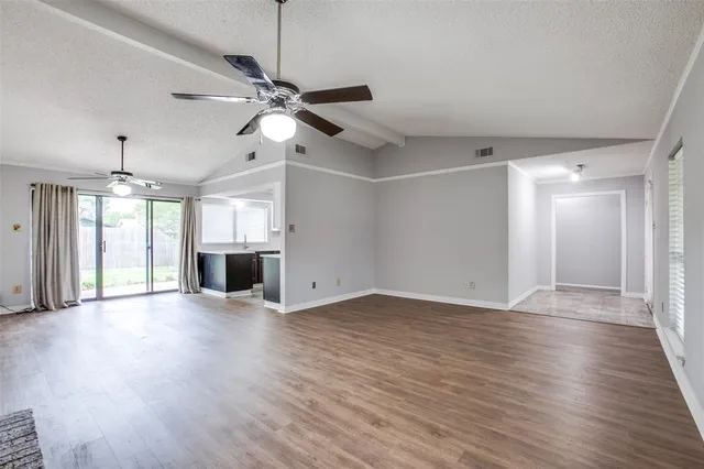 an empty room with wooden floor ceiling fan and windows