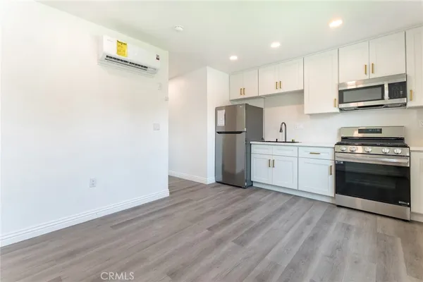 a kitchen with stainless steel appliances a stove top oven a refrigerator and white cabinets with wooden floor