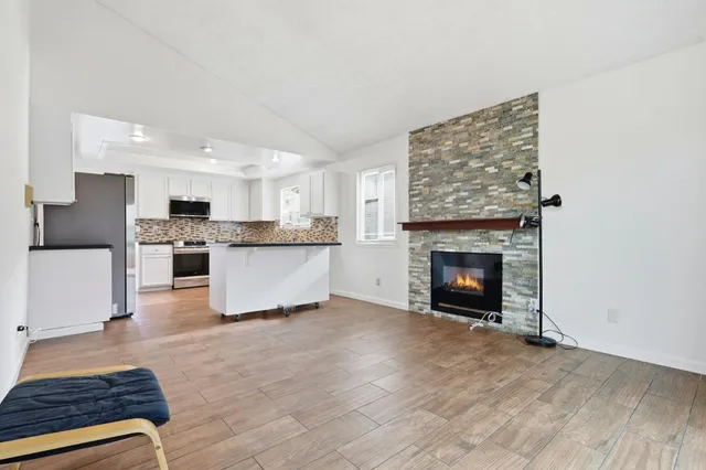 a living room with stainless steel appliances furniture a fireplace and a kitchen view