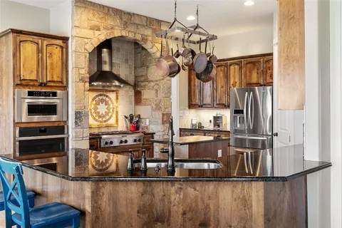 a kitchen with stainless steel appliances granite countertop a refrigerator a stove and a sink with wooden floor