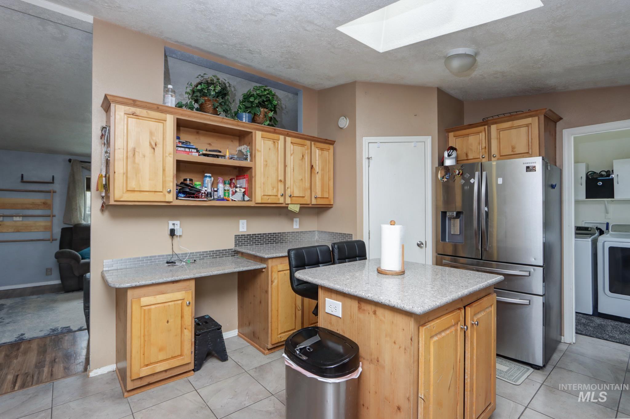 1583 Dustin Lane Vale, OR 97918 - Photo 3 of 39 Kitchen featuring a skylight, stainless steel fridge with ice dispenser, a kitchen island, light tile patterned floors, and light stone countertops